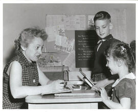 Two children at a library book check out counter with clerk. Part of Jewish Junior Welfare League children libraries project.