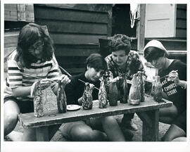 Group portrait of three campers painting bottles as supervisor advises, Camp Wooden Acres, Montreal.