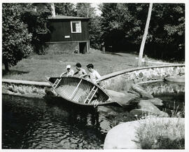 Group portrait of three campers placing canoe in water, Camp Wooden Acres, Montreal.