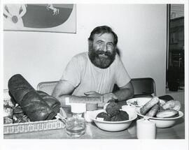 Interior portrait, Alexander Amsel sitting at table, surrounded by some of the baked goods from his restaurant.