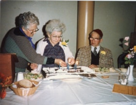 Three unidentified people lighting candles on a cake at a Golden Age Club event