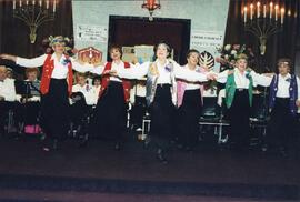 Interior group snapshot, Six unidentified women performing dance in unison at the Cummings Jewish Centre Variety Show, with choir in background.