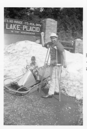 Two unidentified people in front of the Lake Placid sign