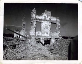 Wall of destroyed building surrounded by rubble, church steeple in background, World War II, France.