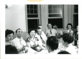 Interior group portrait of men and women seated around a set table. From the collection of the Workmen's Circle.