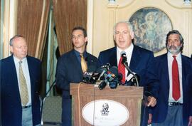 Interior group snapshot, Unidentified man delivering speech at lectern at the Ritz Carlton, Montreal. Standing at left are two unidentified men and one man at right.