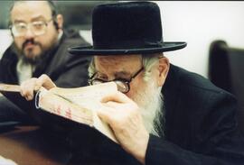 Interior portrait, Rabbi Shloime Goldberg studying Talmud at the Bobover synagogue in Outremont, looking on is Ephraim Katz.
