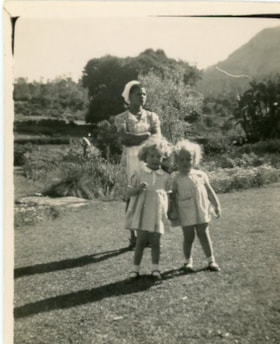 Unidentified twin girls stand outside with an unidentified woman