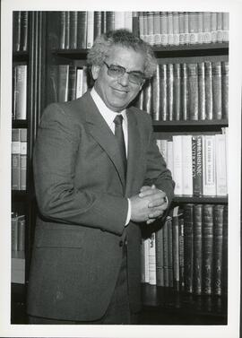Interior portrait, Dr. David Hartman standing in front of bookshelf containing Judaica and Torah books.
