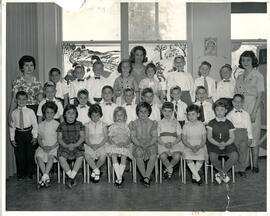 Class photo, interior, Val Royal kindergarten, first row of female students seated on chairs, second row of male students standing, third row of students standing on elevated surface, three teachers standing in back on either side and in middle.